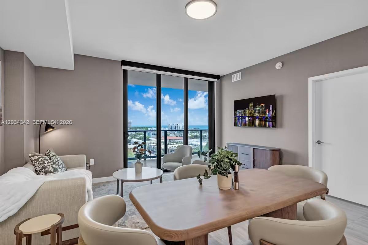 This living and dining area features neutral walls, modern furniture, and floor-to-ceiling windows with views — MIAMI BEACH, FL