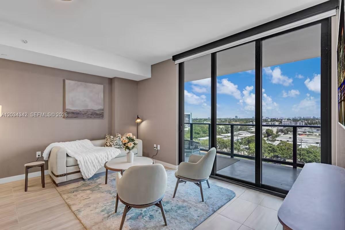 A modern living room features a sofa, two chairs, and floor-to-ceiling windows with balcony access — MIAMI BEACH, FL