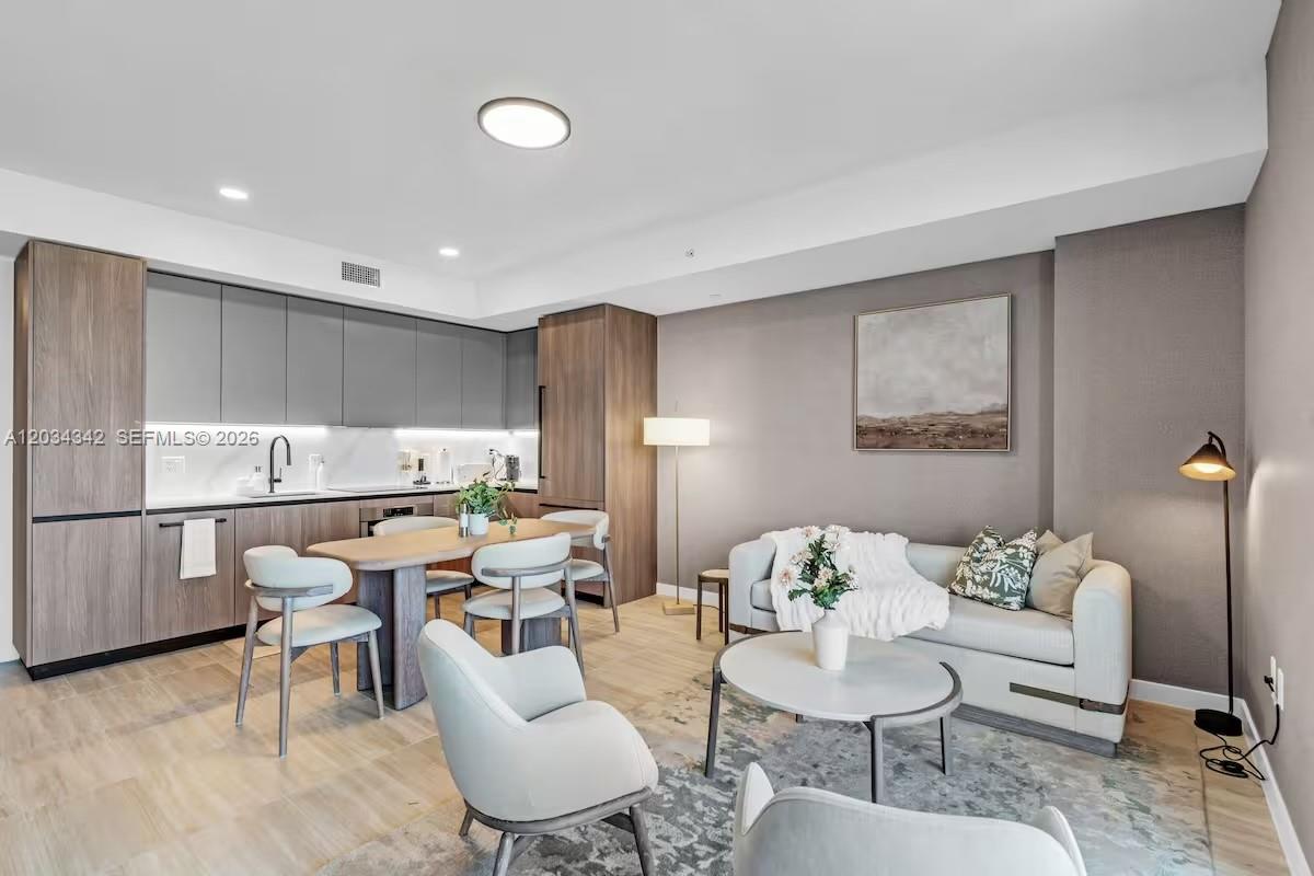 A modern open-concept living room and kitchen feature wood cabinetry, light flooring, and neutral furniture — MIAMI BEACH, FL
