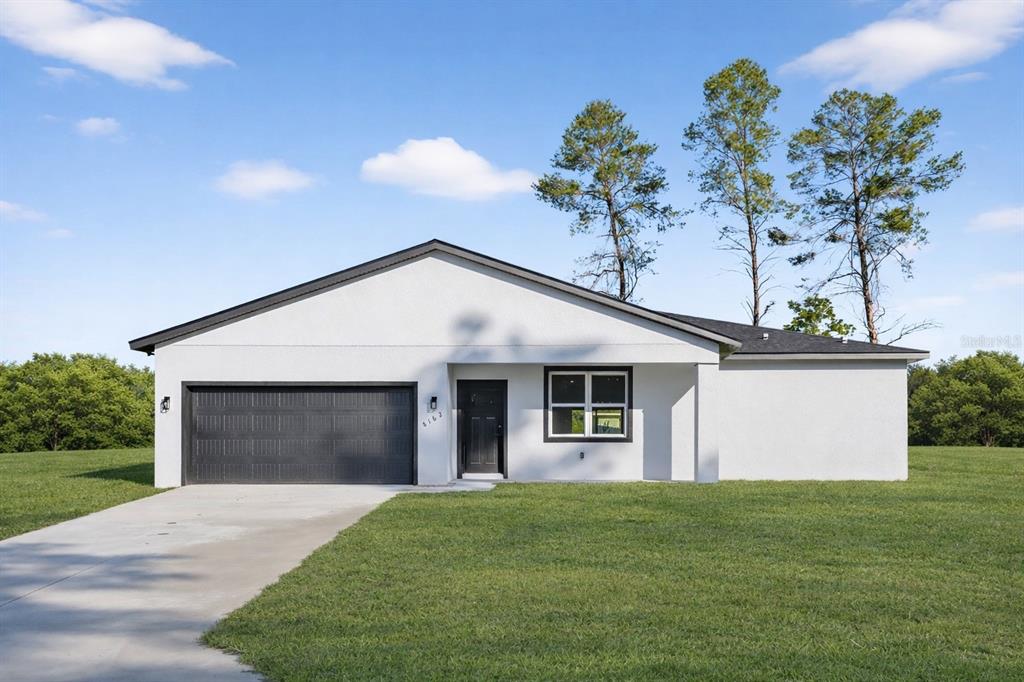 A single-story white house with a black garage door and roof sits on a lawn — 8162 N MALTESE DRIVE, CITRUS SPRINGS, FL