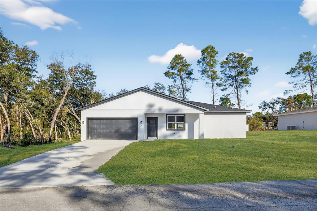 A single-story white house with a dark garage door and front door sits on grass — 8162 N MALTESE DRIVE, CITRUS SPRINGS, FL