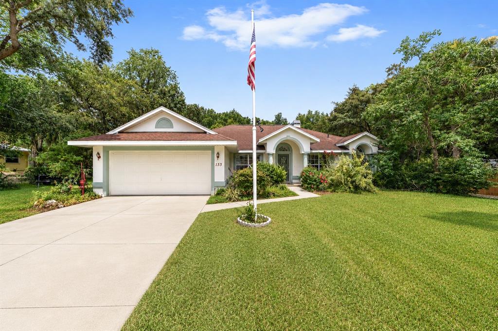 A single-story house with a white garage, a front lawn, and a tall flagpole — 133 N MCGOWAN, CRYSTAL RIVER, FL