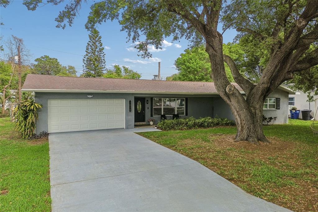 A single-story gray house with a two-car garage, a large oak tree, and a driveway — 1618 BARRY ROAD, CLEARWATER, FL