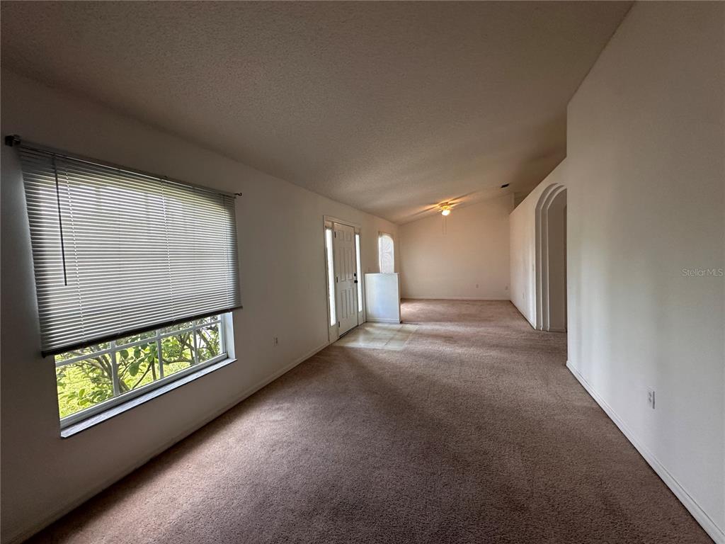 A carpeted living room features a large window with blinds and an arched entryway — 33 RYBARK LANE, PALM COAST, FL