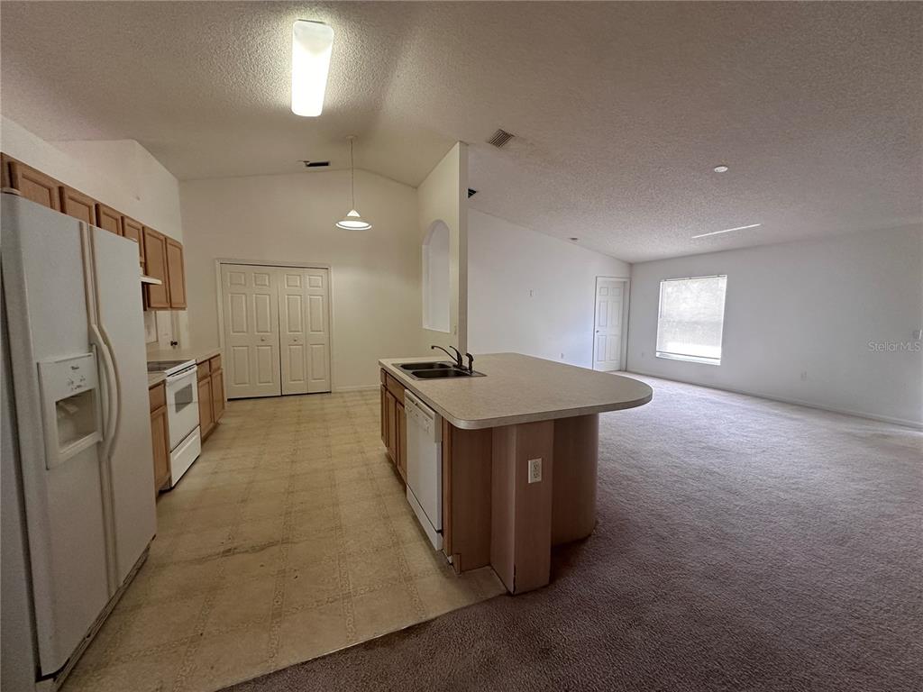 A kitchen with light wood cabinets and an island opens into a carpeted living area — 33 RYBARK LANE, PALM COAST, FL
