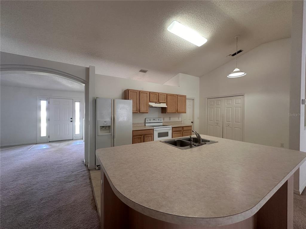 A kitchen with a central island, light-colored countertops, and wooden cabinets overlooks an entryway — 33 RYBARK LANE, PALM COAST, FL