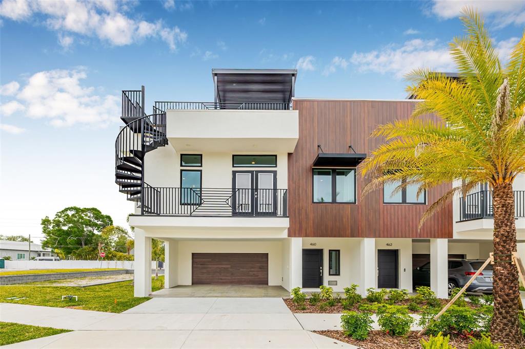 A modern three-story townhouse features a spiral staircase, wood-paneled siding, and a ground-level garage — 490 87TH AVENUE NORTH, ST PETERSBURG, FL