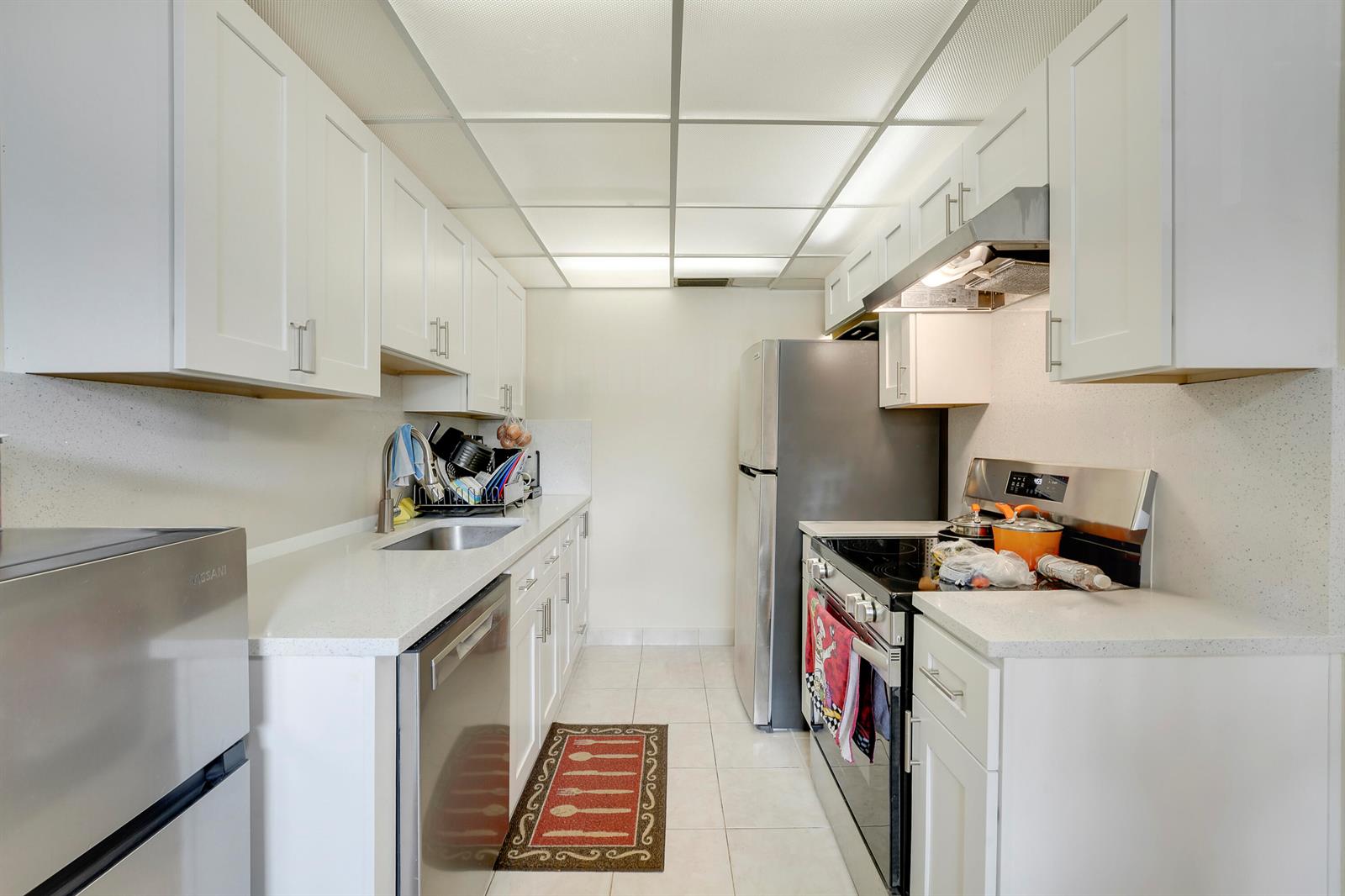 A galley kitchen features white cabinets, stainless steel appliances, and light-colored countertops — 1011 Exeter, Boca Raton FL 33434, BOCA RATON, FL