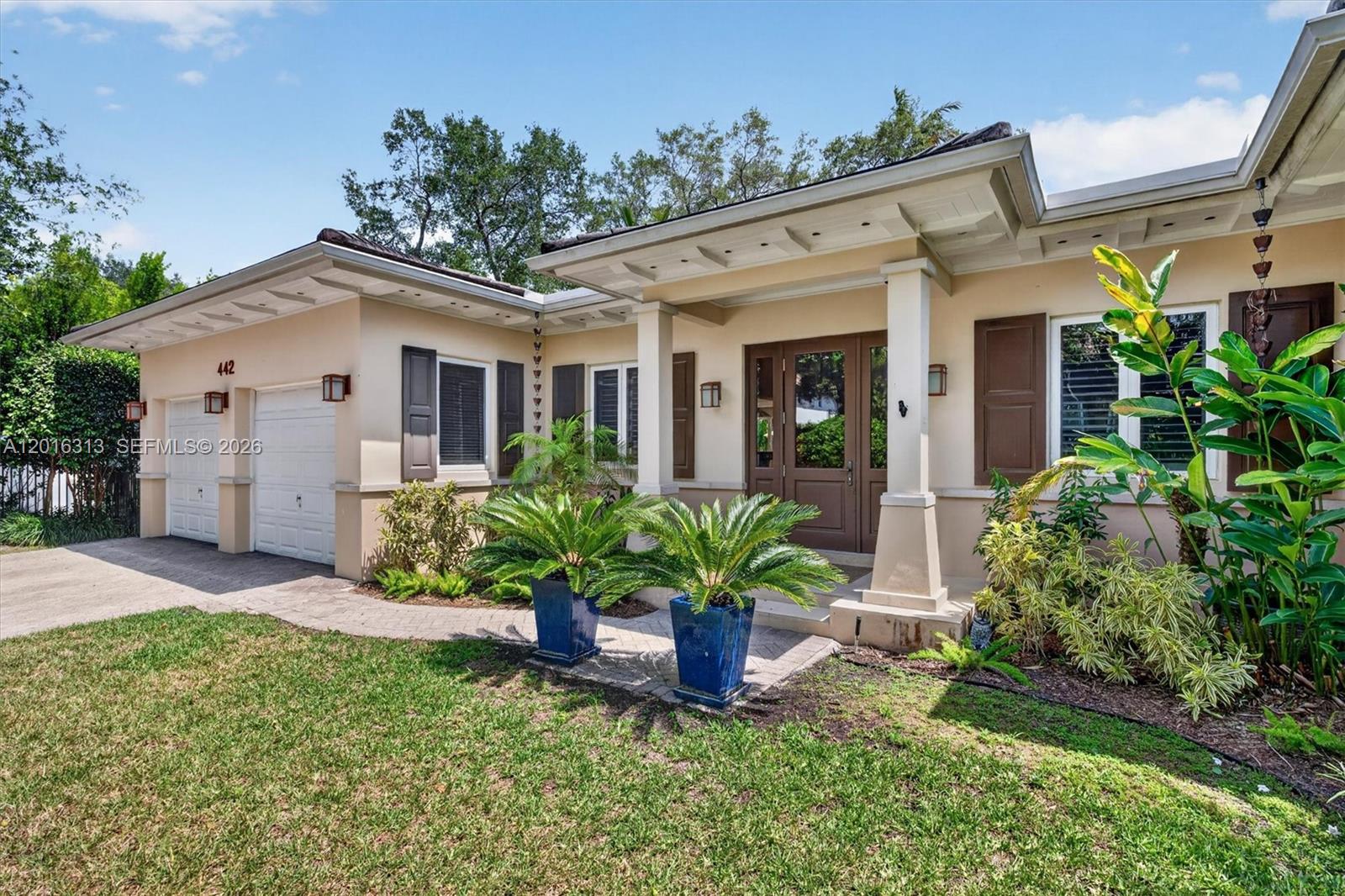 The exterior of a single-story house features a two-car garage, a covered entryway, and landscaping — 442 Amalfi Ave, Coral Gables FL 33146, CORAL GABLES, FL