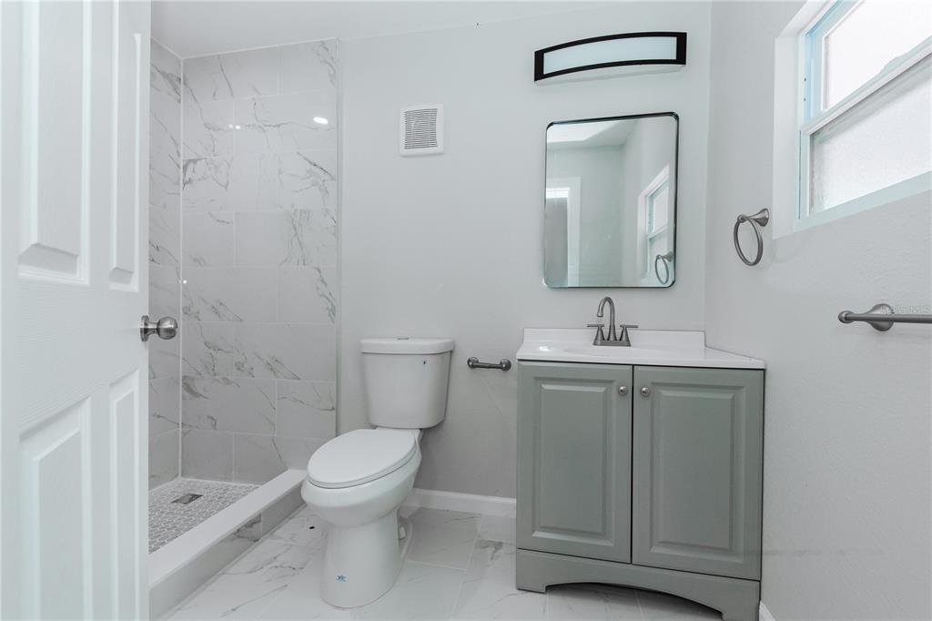 A modern bathroom features a walk-in shower, a gray vanity, and white marble-look tile flooring — 2240 10TH STREET S, ST PETERSBURG, FL