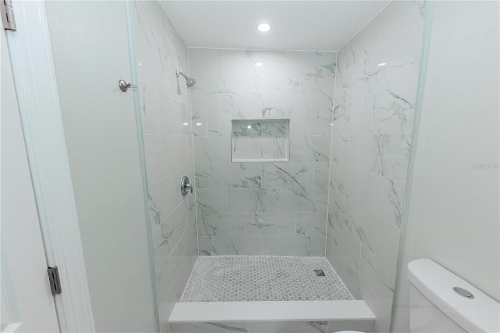 A walk-in shower features white marble-look wall tiles, a pebble floor, and a recessed niche — 2240 10TH STREET S, ST PETERSBURG, FL