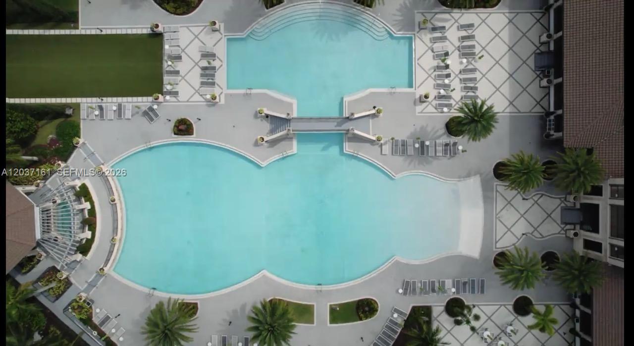 An aerial view shows a large, uniquely shaped swimming pool with a central pedestrian bridge — 7661 NW 103rd Ct, Doral FL 33178, DORAL, FL