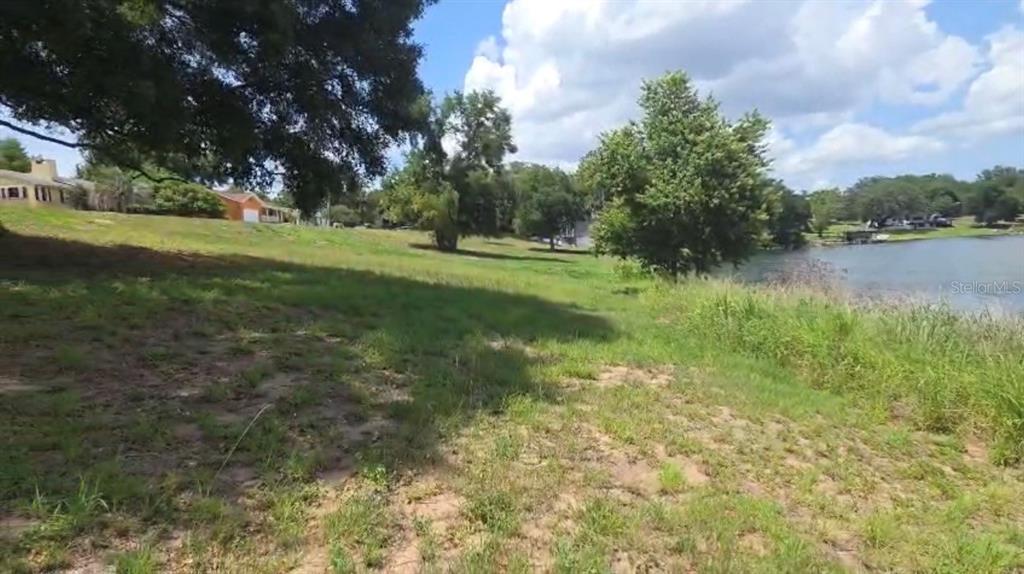 A grassy, sloped lot leads down to a lake with trees and houses nearby — 0 S LAKESHORE COURT, EUSTIS, FL