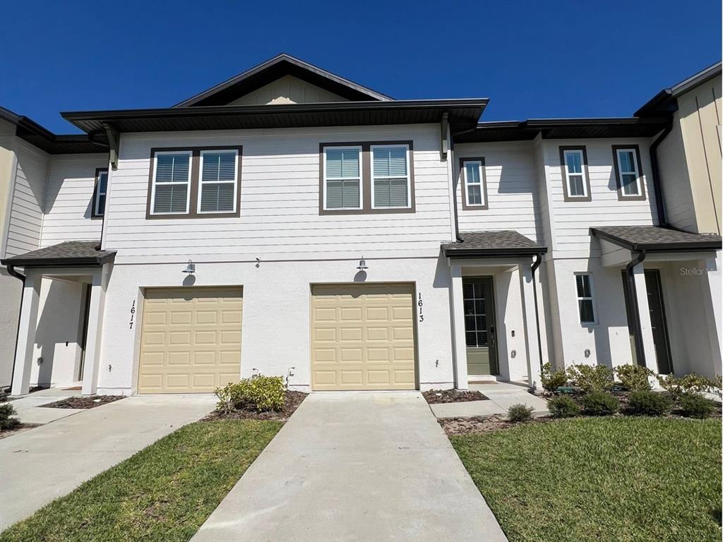 A two-story townhouse exterior features white horizontal siding, two tan garage doors, and a driveway — 1613 PELICAN DRIVE, DAVENPORT, FL