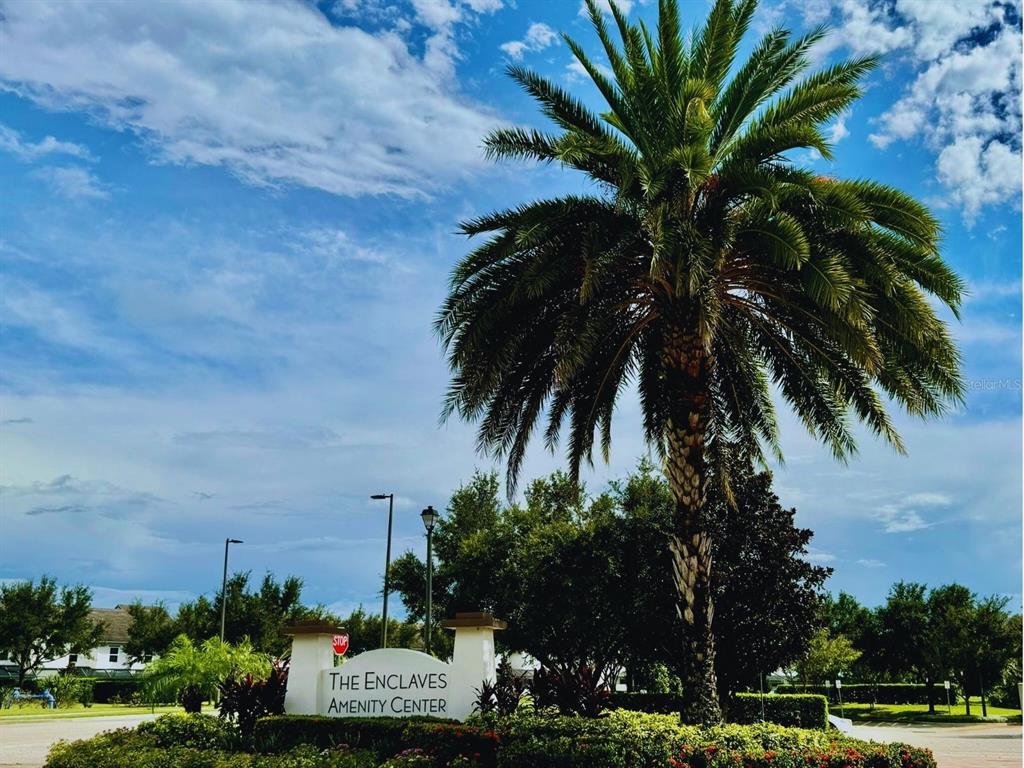 A palm tree stands behind a sign for The Enclaves Amenity Center under a blue sky — 1613 PELICAN DRIVE, DAVENPORT, FL