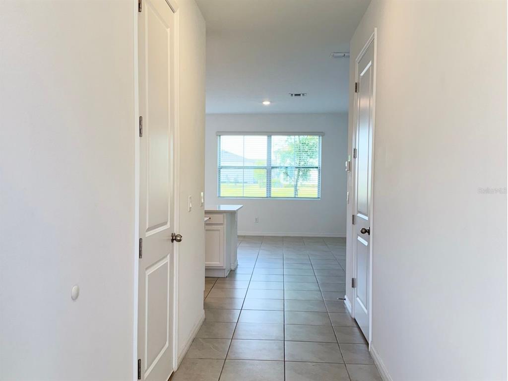 A hallway with tile flooring leads to an open kitchen area with a large window — 1613 PELICAN DRIVE, DAVENPORT, FL