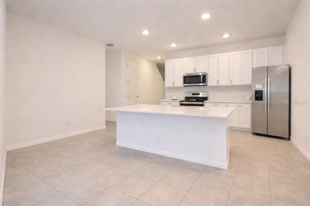 A kitchen features white cabinets, stainless steel appliances, a central island, and light tile flooring — 1613 PELICAN DRIVE, DAVENPORT, FL