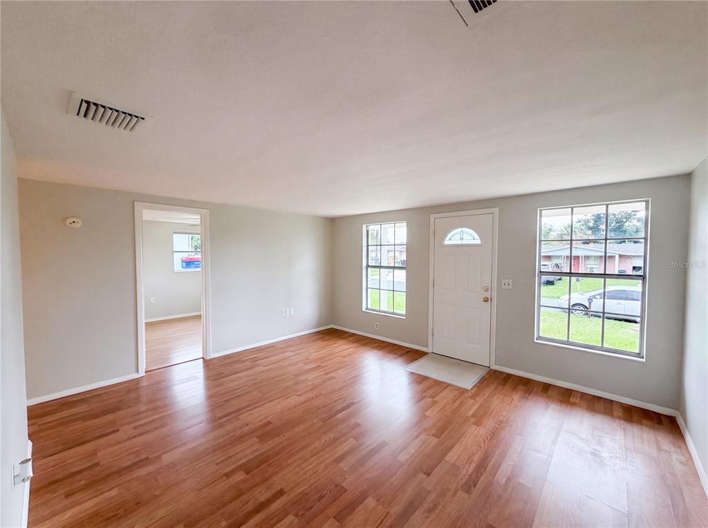 An empty living room features light gray walls, wood-look flooring, a front door, and windows — 4639 IRENE LOOP, NEW PORT RICHEY, FL