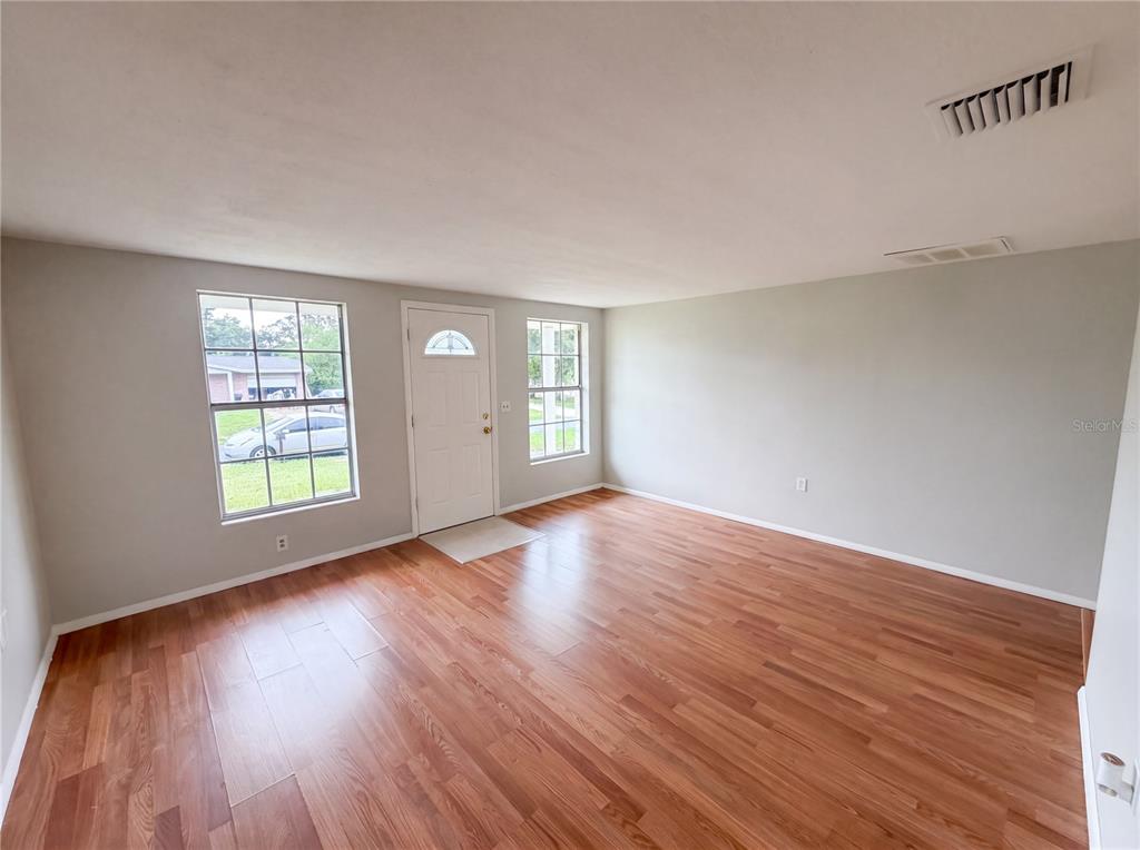 An empty room features light gray walls, wood-look flooring, two windows, and a white front door — 4639 IRENE LOOP, NEW PORT RICHEY, FL