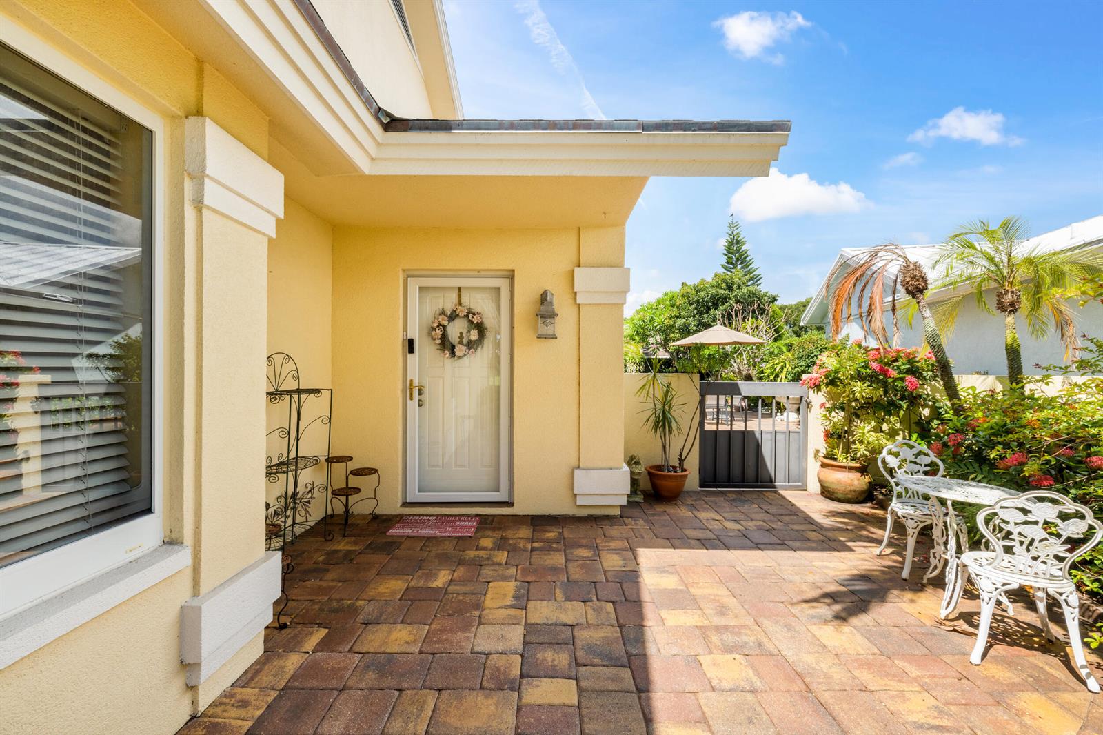 A yellow house exterior features a paved patio, a white front door, and patio furniture — 224 Cape Pointe Circle, Jupiter FL 33477, JUPITER, FL