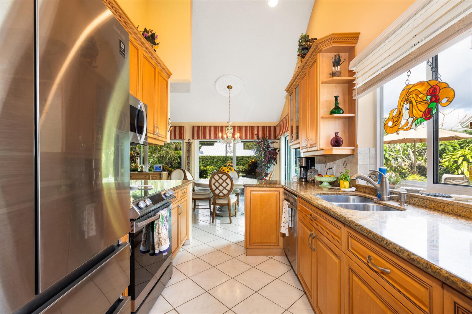 A kitchen with wood cabinets, granite countertops, and stainless steel appliances leads to a dining area — 224 Cape Pointe Circle, Jupiter FL 33477, JUPITER, FL