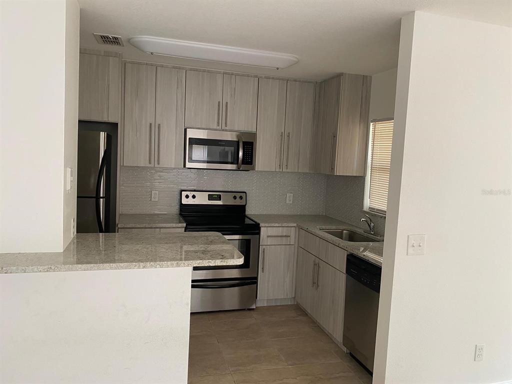 A kitchen features light wood-grain cabinets, granite countertops, and stainless steel appliances — 5452 E MICHIGAN STREET UNIT 5452-1, ORLANDO, FL