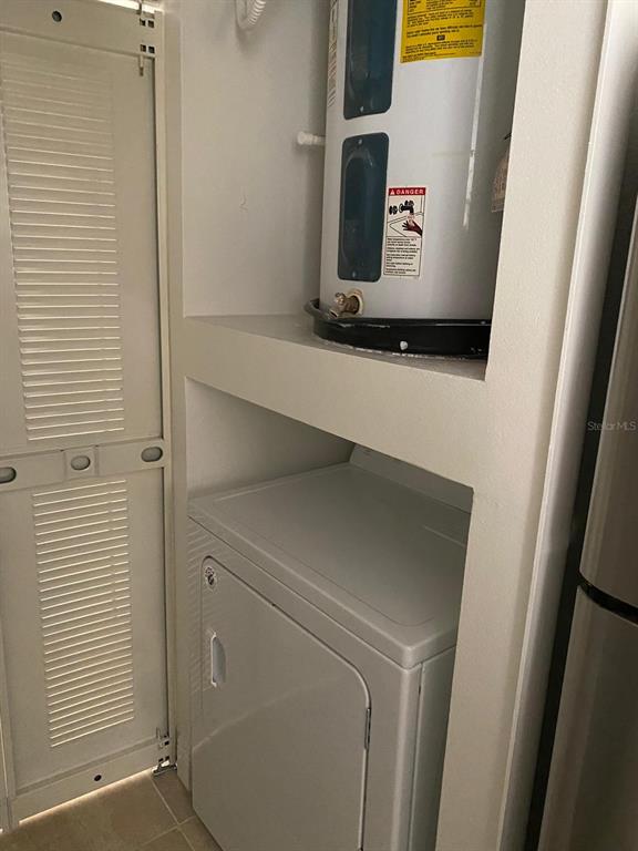 A water heater sits on a shelf above a clothes dryer in a utility closet — 5452 E MICHIGAN STREET UNIT 5452-1, ORLANDO, FL