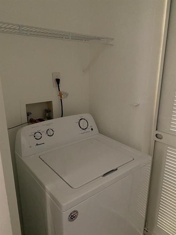 A white top-loading Amana washing machine sits in a laundry closet with a wire shelf — 5452 E MICHIGAN STREET UNIT 5452-1, ORLANDO, FL