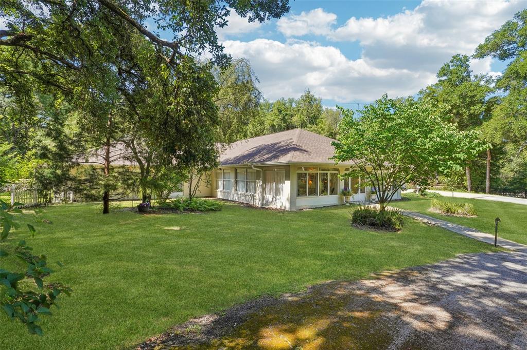 A single-story house with a light-colored exterior sits on a large, grassy, tree-filled lot — 4546 GRIFFIN VIEW DRIVE, LADY LAKE, FL