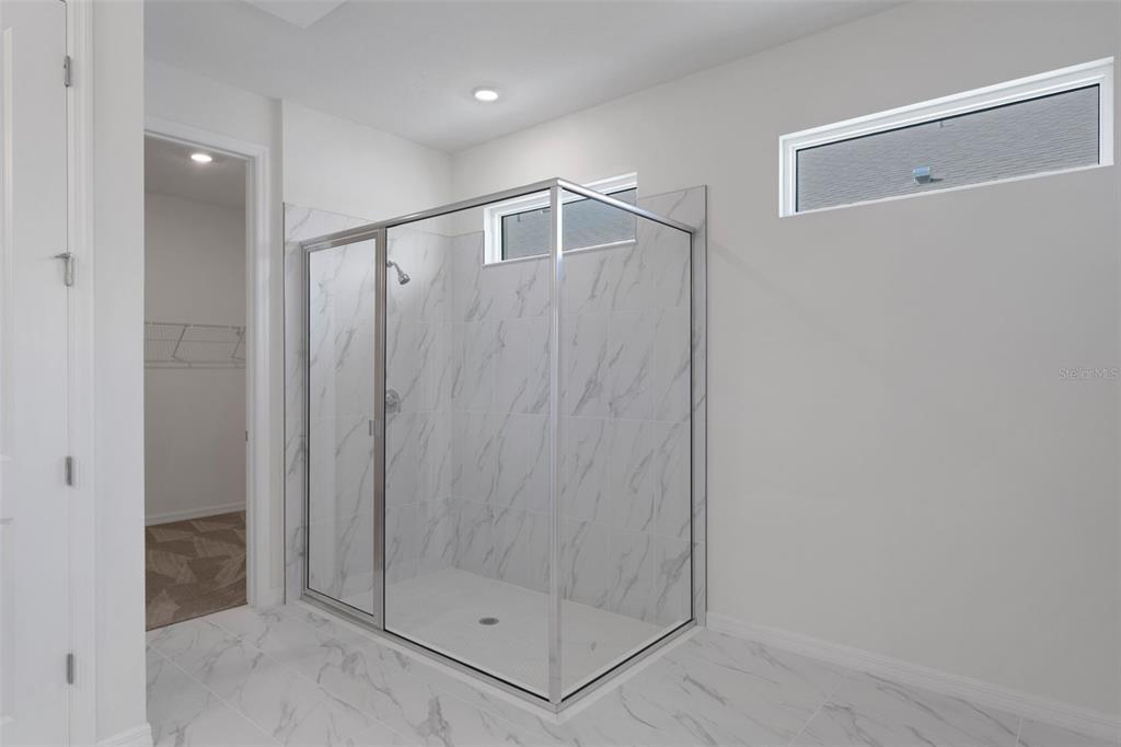A walk-in shower with marble-look tile and a glass enclosure stands in a bathroom — 17013 GREAT HERON LANE, PUNTA GORDA, FL