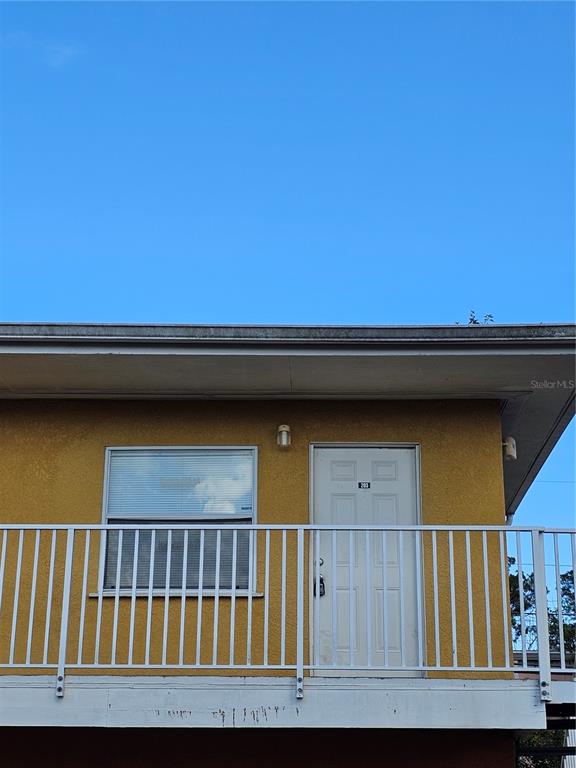 A yellow exterior wall features a window and a white door with a balcony railing — 119 N EVERGREEN AVENUE UNIT 203, CLEARWATER, FL