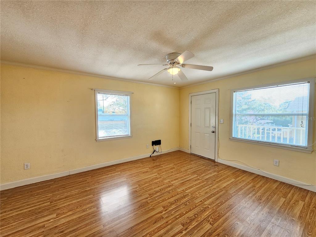 An empty room features yellow walls, wood-look flooring, a ceiling fan, and two windows — 119 N EVERGREEN AVENUE UNIT 203, CLEARWATER, FL