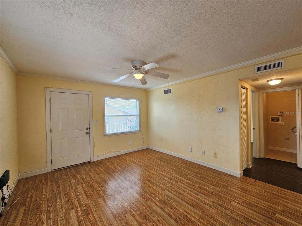 A living room with yellow walls, wood-look flooring, a ceiling fan, and an exterior door — 119 N EVERGREEN AVENUE UNIT 203, CLEARWATER, FL