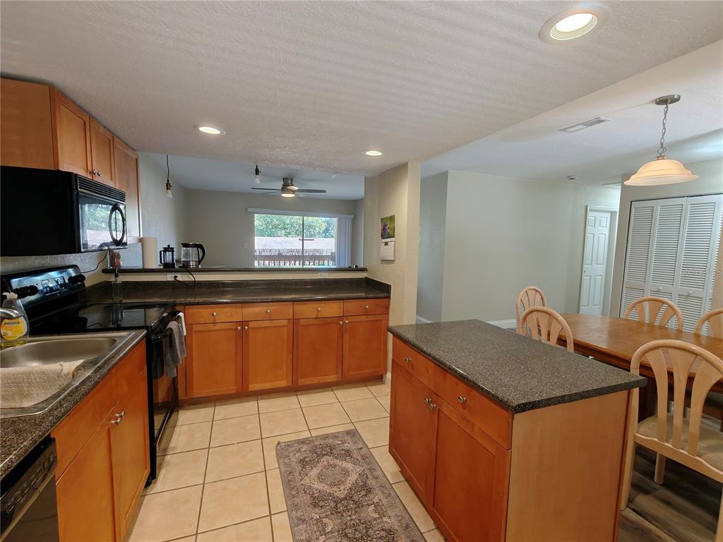 A kitchen features wood cabinets, dark countertops, tile flooring, and an island with seating — 1810 NW 23RD BOULEVARD UNIT 165, GAINESVILLE, FL