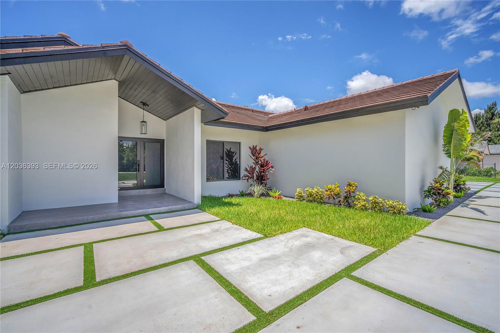 The exterior of a white house features a modern concrete paver driveway with grass joints — 16100 SW 252nd St, Homestead FL 33031, HOMESTEAD, FL