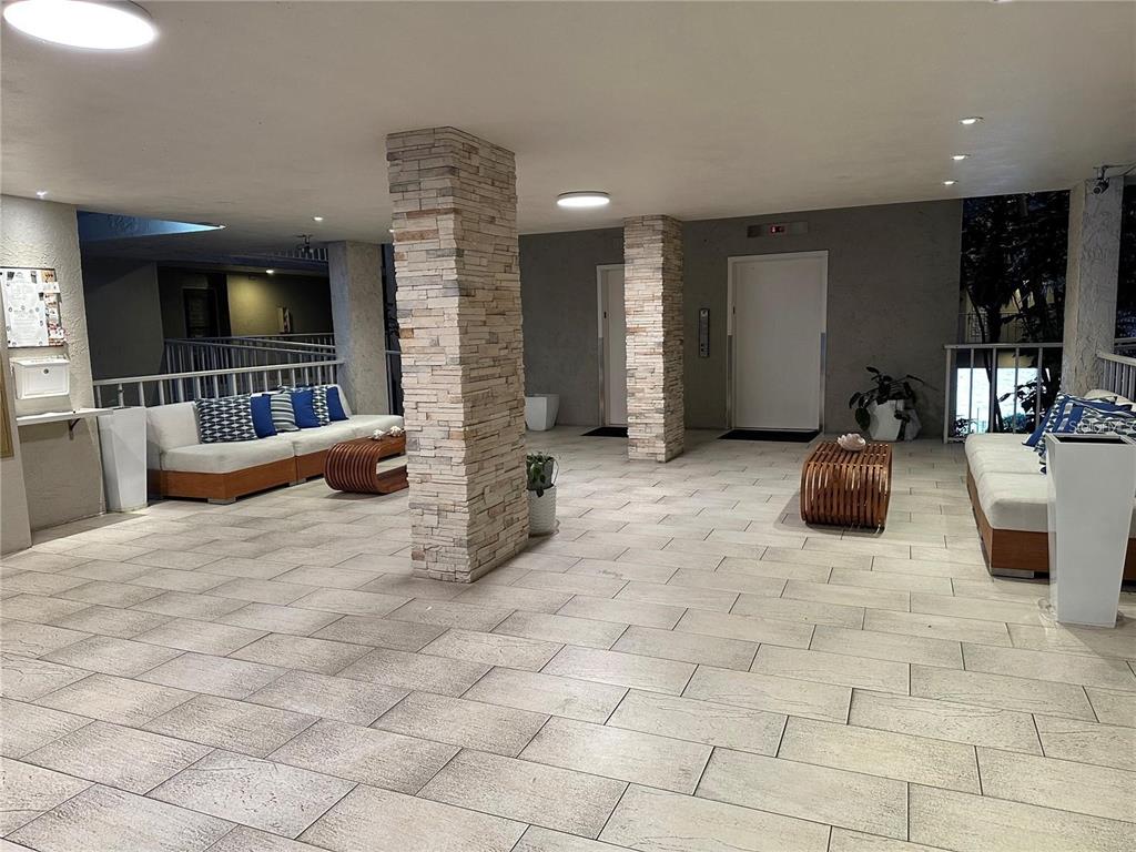 An open-air lobby features stone-clad pillars, tile flooring, and two seating areas with white sofas — 500 N OSCEOLA AVENUE UNIT 403, CLEARWATER, FL