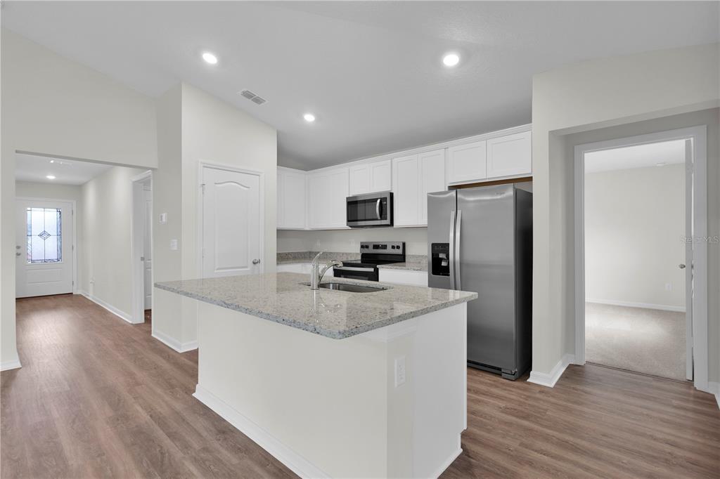 A kitchen features a granite-topped island, white cabinetry, stainless steel appliances, and wood-look flooring — 15777 SW 23RD COURT ROAD, OCALA, FL