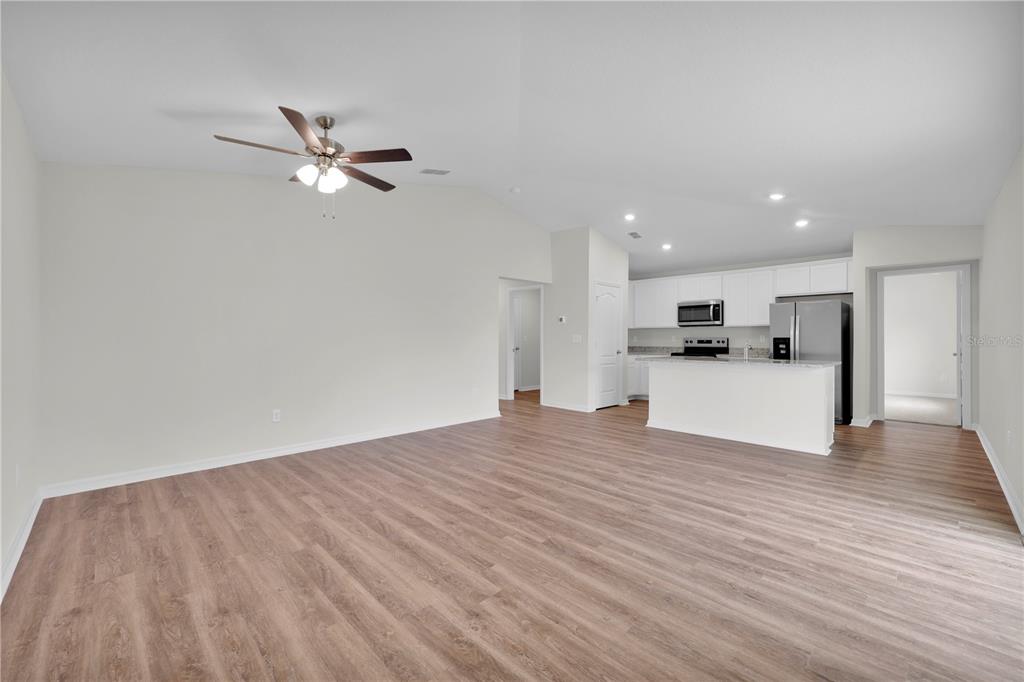 An open-concept living area features light wood-look flooring, a ceiling fan, and a white kitchen — 15777 SW 23RD COURT ROAD, OCALA, FL