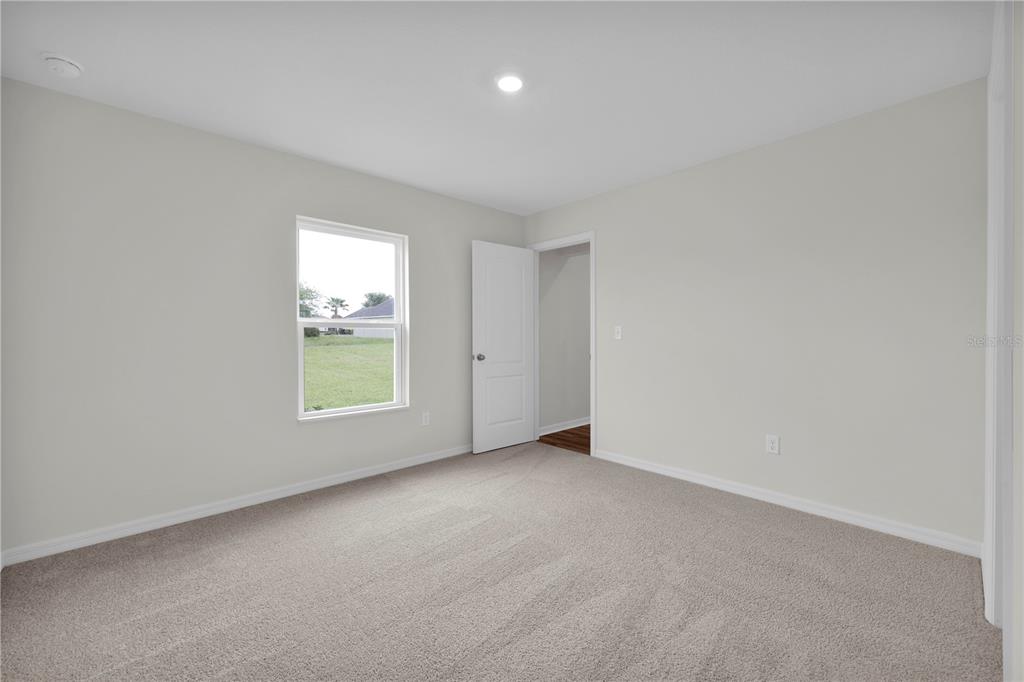 A bedroom with beige carpet, light-colored walls, a single window, and an open doorway — 15777 SW 23RD COURT ROAD, OCALA, FL