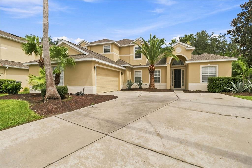 A two-story suburban house with a tan stucco exterior, a two-car garage, and palm trees — 3469 FOREST RIDGE LANE, KISSIMMEE, FL