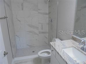 A bathroom features a walk-in shower with marble-look tile, a toilet, and a granite vanity — 1 FISHER TERRACE TRACE UNIT 201, OCKLAWAHA, FL