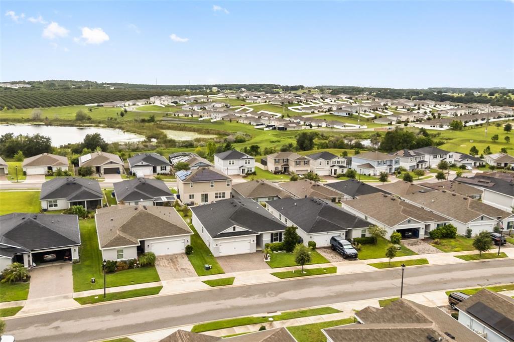 An aerial view shows a suburban neighborhood with houses, green lawns, and a nearby pond — 1731 WILSON PRAIRIE CIRCLE, GROVELAND, FL