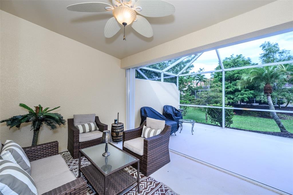 A covered patio features wicker furniture, a ceiling fan, and a screened-in view of trees — 327 MONACO DRIVE UNIT 12, PUNTA GORDA, FL