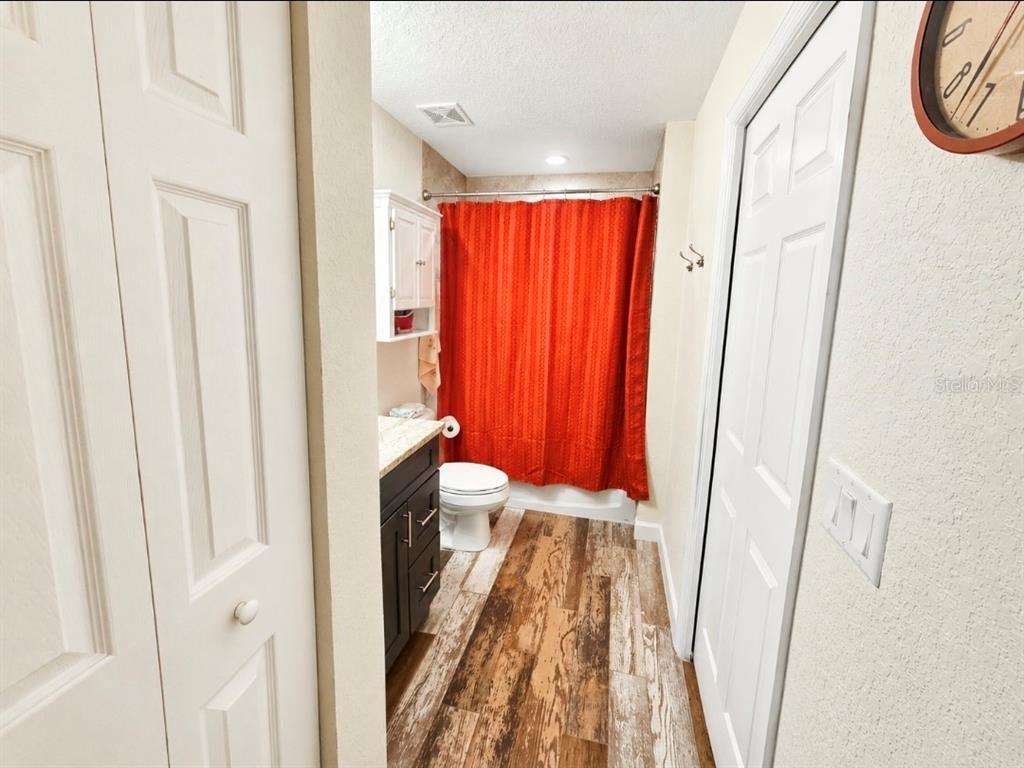 A bathroom features wood-look tile flooring, a dark vanity, and a bright orange shower curtain — 3805 SW 115TH STREET, OCALA, FL