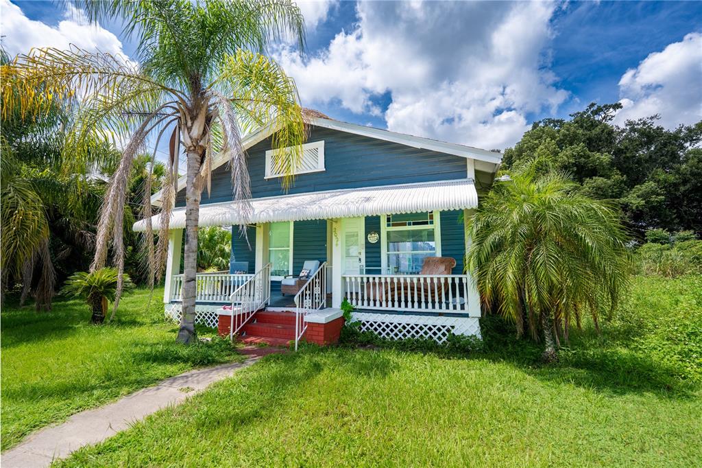 A blue house with a white porch, metal awning, and palm trees in the yard — 2024 OLD LAKE MARY ROAD, SANFORD, FL