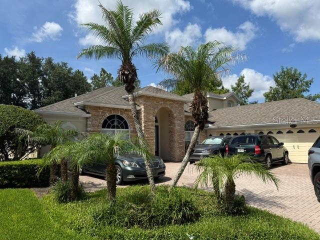 A single-story house with a stone facade, palm trees, and two cars in the driveway — 13856 GLYNSHEL DRIVE, WINTER GARDEN, FL