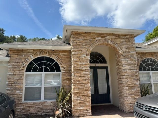 The exterior of a stone-faced house features an arched entryway and two arched windows — 13856 GLYNSHEL DRIVE, WINTER GARDEN, FL