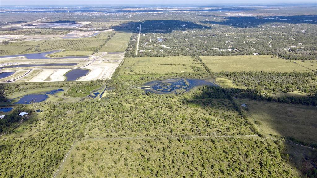 An aerial view shows a large, undeveloped plot of land with trees, ponds, and fields — 14266 BURNT STORE ROAD, PUNTA GORDA, FL