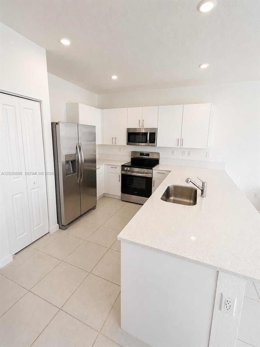 A modern kitchen features white cabinetry, stainless steel appliances, and a large quartz-topped island — 2840 SE 26th Ter, Homestead FL 33035, HOMESTEAD, FL
