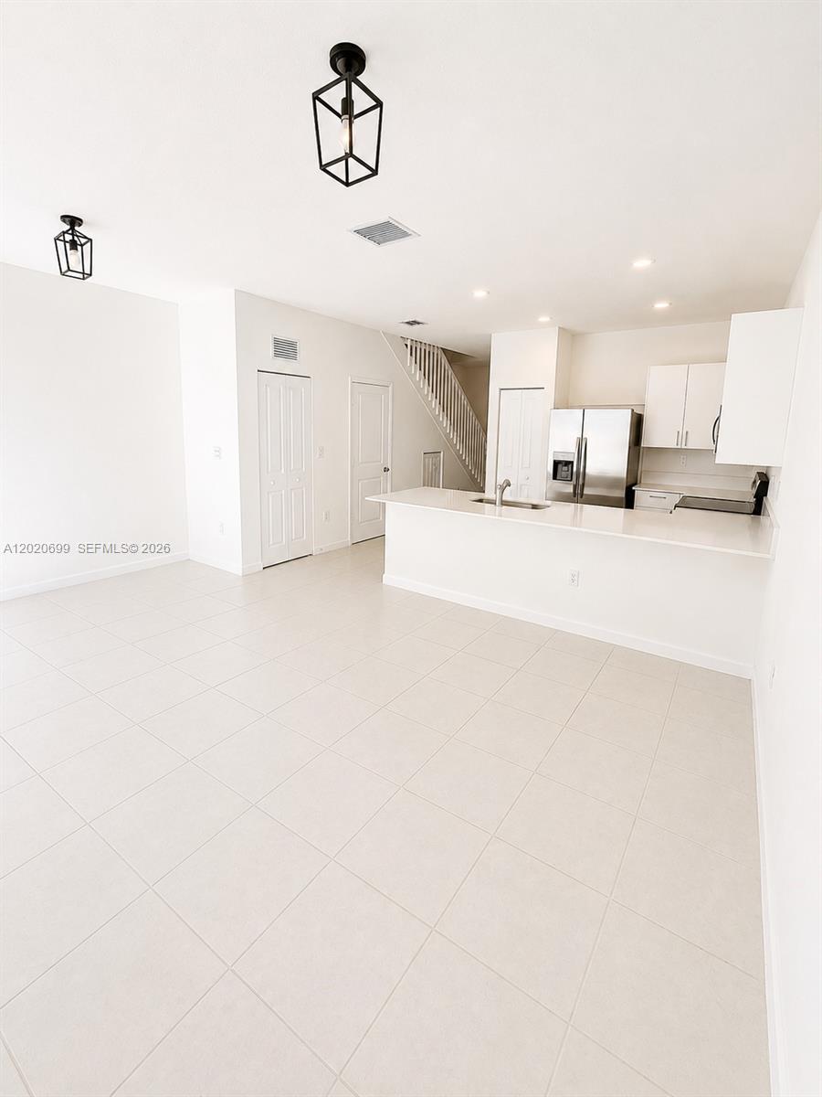 This open-concept kitchen and living area features white cabinetry, stainless steel appliances, and tile flooring — 2840 SE 26th Ter, Homestead FL 33035, HOMESTEAD, FL